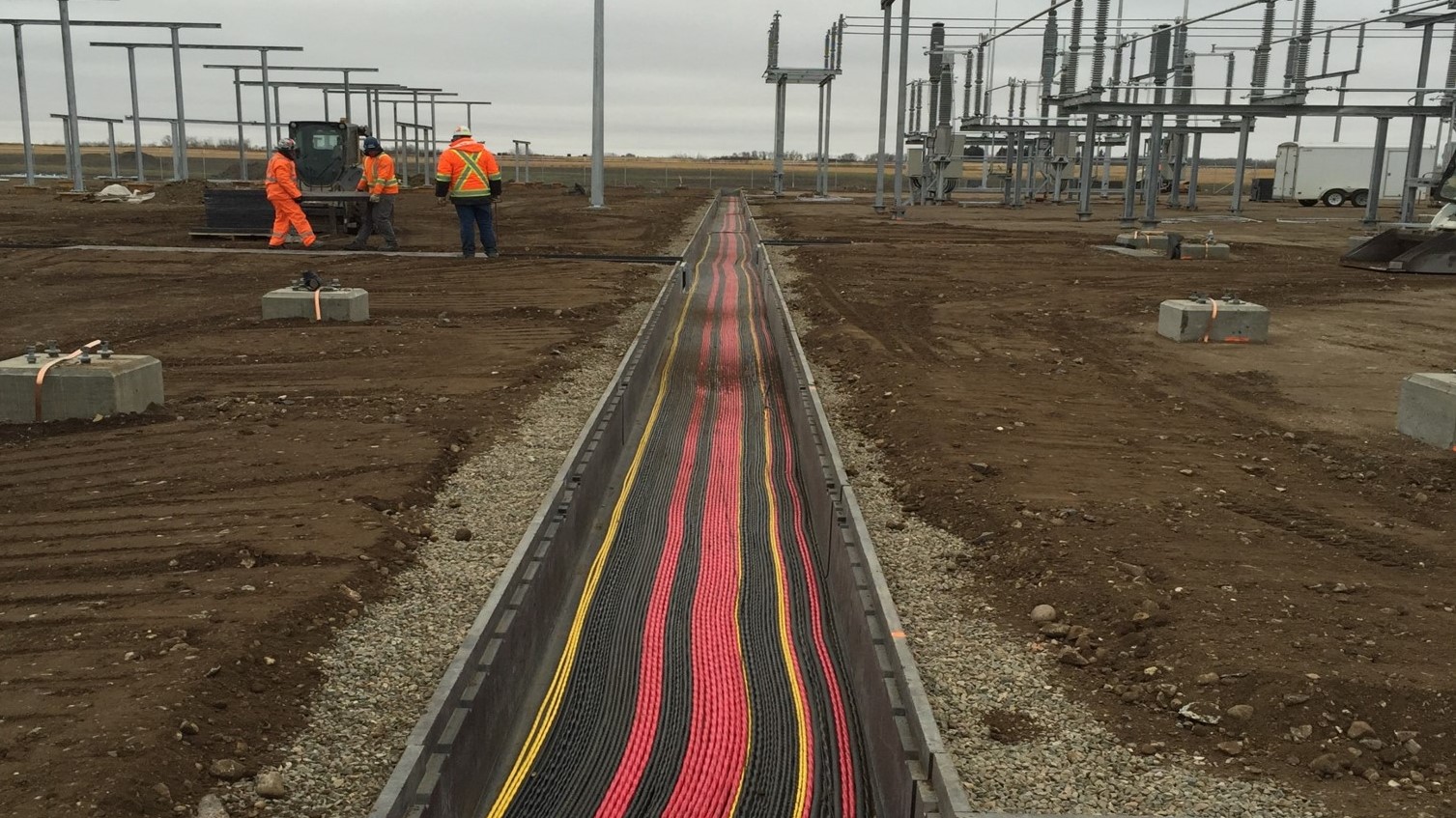  Dynamo employees cover the electrical wire-filled trench in preparation for substation construction. All three employees are wearing Personal Protective safety equipment.