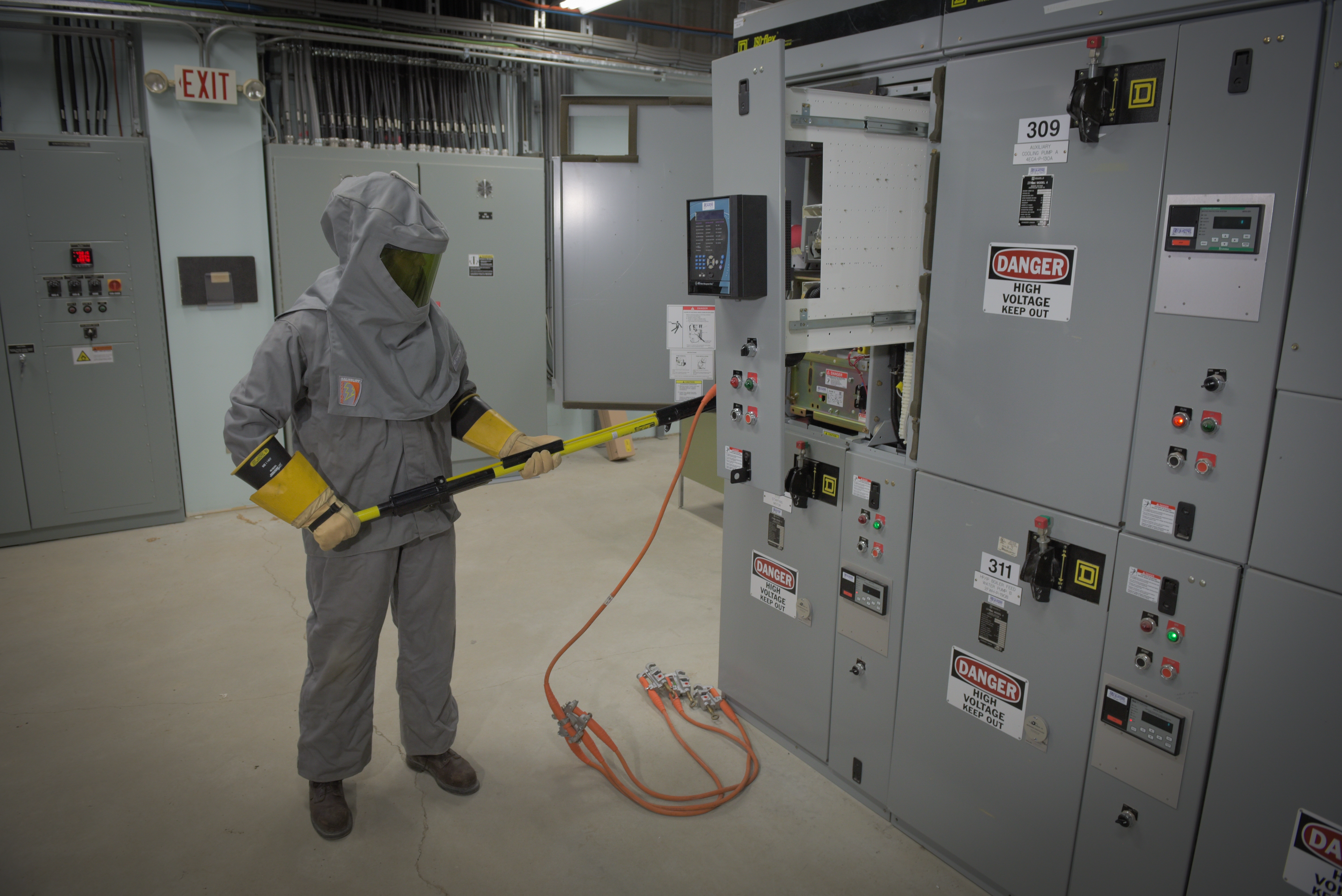 Dynamo employee using High voltage hot stick to minimize risk to person and equipment. The employee is in full protective arc flash suit.