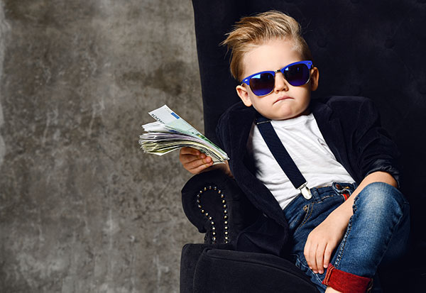 little boy sitting on a chair with his legs crossed holding a stack of cash and wearing sunglasses